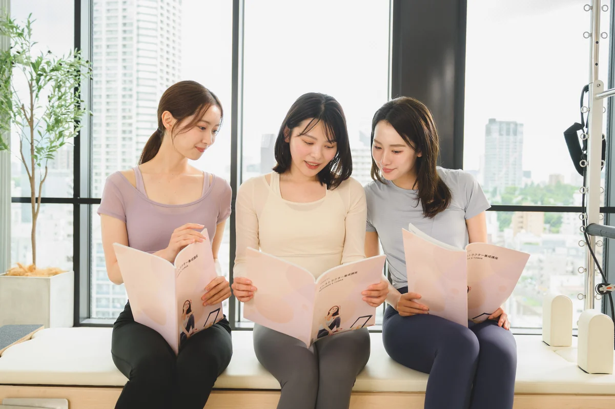 研修でテキストを読み合い、笑顔で話す3人の受講者
